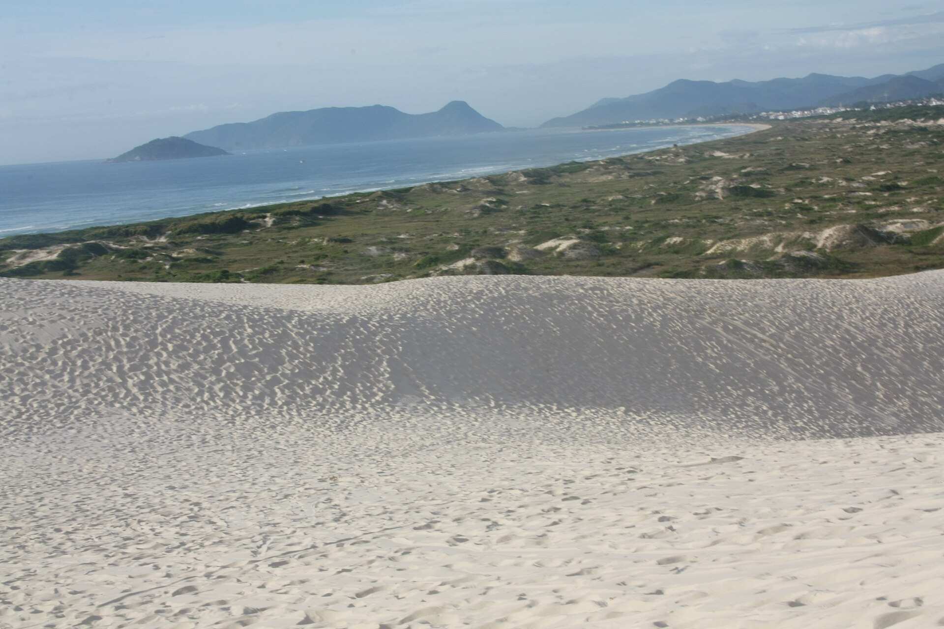 Duna de areia clara nas Dunas da Joaquina, com a praia e a Ilha do Campeche ao fundo